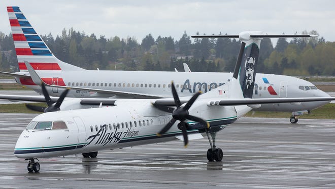 An Alaska Airlines Q400 turboprop pulls into a gate while an American Airlines Boeing 737-800 heads out for takeoff in Seattle.