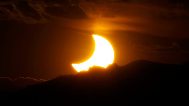 In this May 20, 2012, file photo, a solar eclipse is seen from downtown Denver as the sun sets behind the Rocky Mountains.