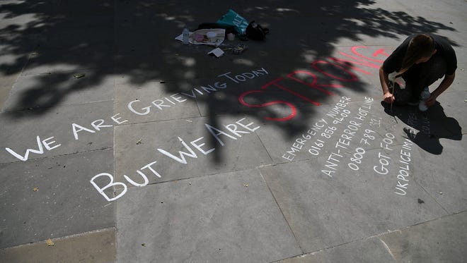 A young man writes emergency details and a tribute message on a sidewalk on May 23, 2017, in Manchester, England.