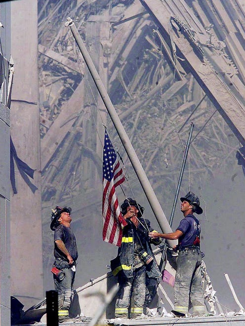 Brooklyn firefighters George Johnson, left, of ladder 157, Dan McWilliams, center, of ladder 157, and  Billy Eisengrein, right, of Rescue 2, raise a flag at the World Trade Center site in New York.