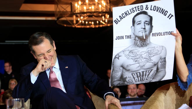 Cruz laughs at a poster while speaking to guests at a town hall event on March 30, 2016, in Madison, Wis.