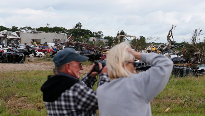 People look and take photos of cars and damaged material seen piled up at a local car dealership that was destroyed when a large tornado hit the area near Canton, Texas on April 30, 2017. Five people are reported killed from the severe weather that has hit areas across Texas and surrounding states.