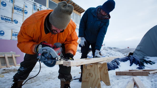 Matt Yerge from Buffalo, NY, cuts a stud for a winter home as Terrance Hubbard of Clevland looks in the Oceti Sakowin Camp near the Standing Rock Reservation on Saturday, Dec. 3, 2016 near Cannon Ball. The home is being built for native families who don't have a proper winter structure they said.