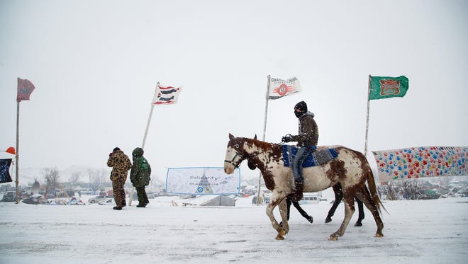 A rider on horseback rides up Flag Row as snow falls on the Oceti Sakowin Camp on Monday, Dec. 5, 2016, near Cannon Ball.