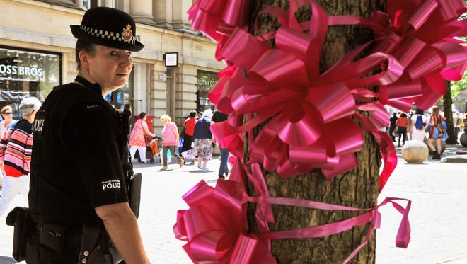 Police patrol past a pink ribbon tribute in central Manchester, England.