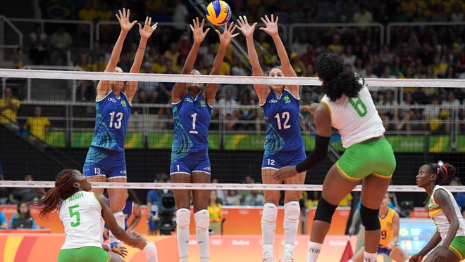 Brazil outside hitter Sheilla Castro de Paula Blassioli (13), middle blocker Fabiana Claudino (1), and weak side hitter Natalia Pereira (12) work to block a shot by Cameroon weak side hitter Laetitia Crescence Moma Bassoko during their game in the preliminary round in the Rio 2016 Summer Olympic Games at Maracanazinho.