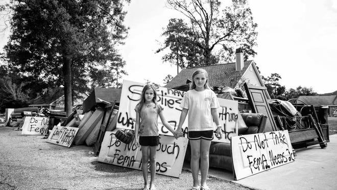 Friends, Zoey & Katelynn hold hands in their neighborhood surrounded by debris. Signs are popping up asking people to leave their belongings in the yard, residents fear getting shorted by FEMA if they can't prove their losses. Watson, LA.