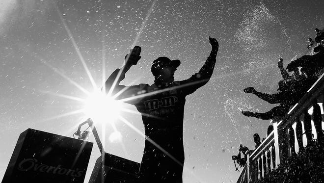 This black and white image shows Kyle Busch basking in his first career Cup win at Pocono Raceway as fans spray him from along the rail atop victory lane on July 30.