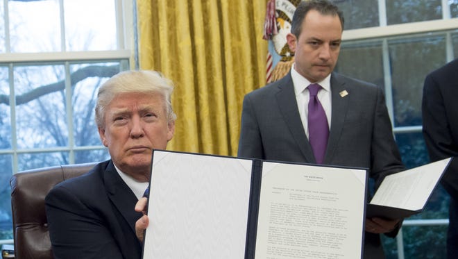 President Trump holds up an executive order withdrawing the US from the Trans-Pacific Partnership after signing it alongside White House Chief of Staff Reince Priebus in the Oval Office Monday.